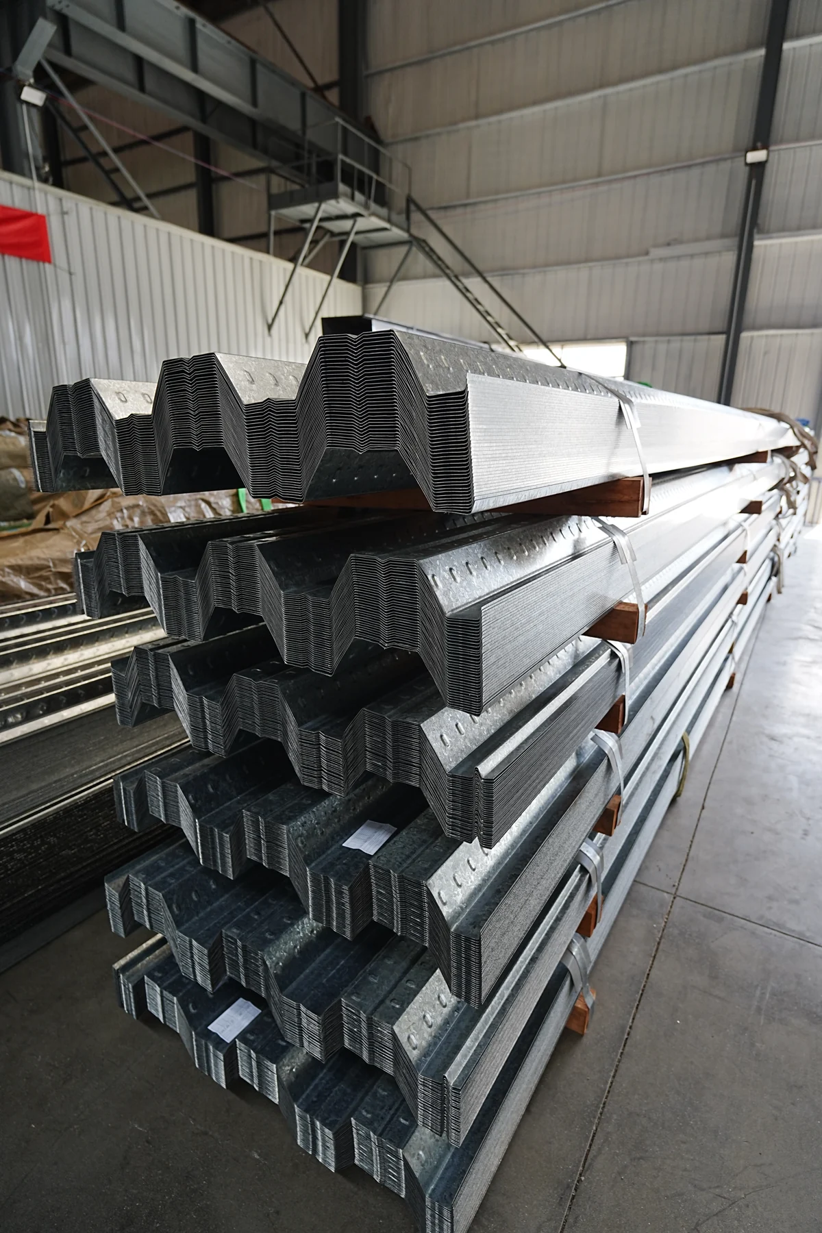 Stacked galvanized profiled steel floor deck sheets with visible rib geometry in a workshop
